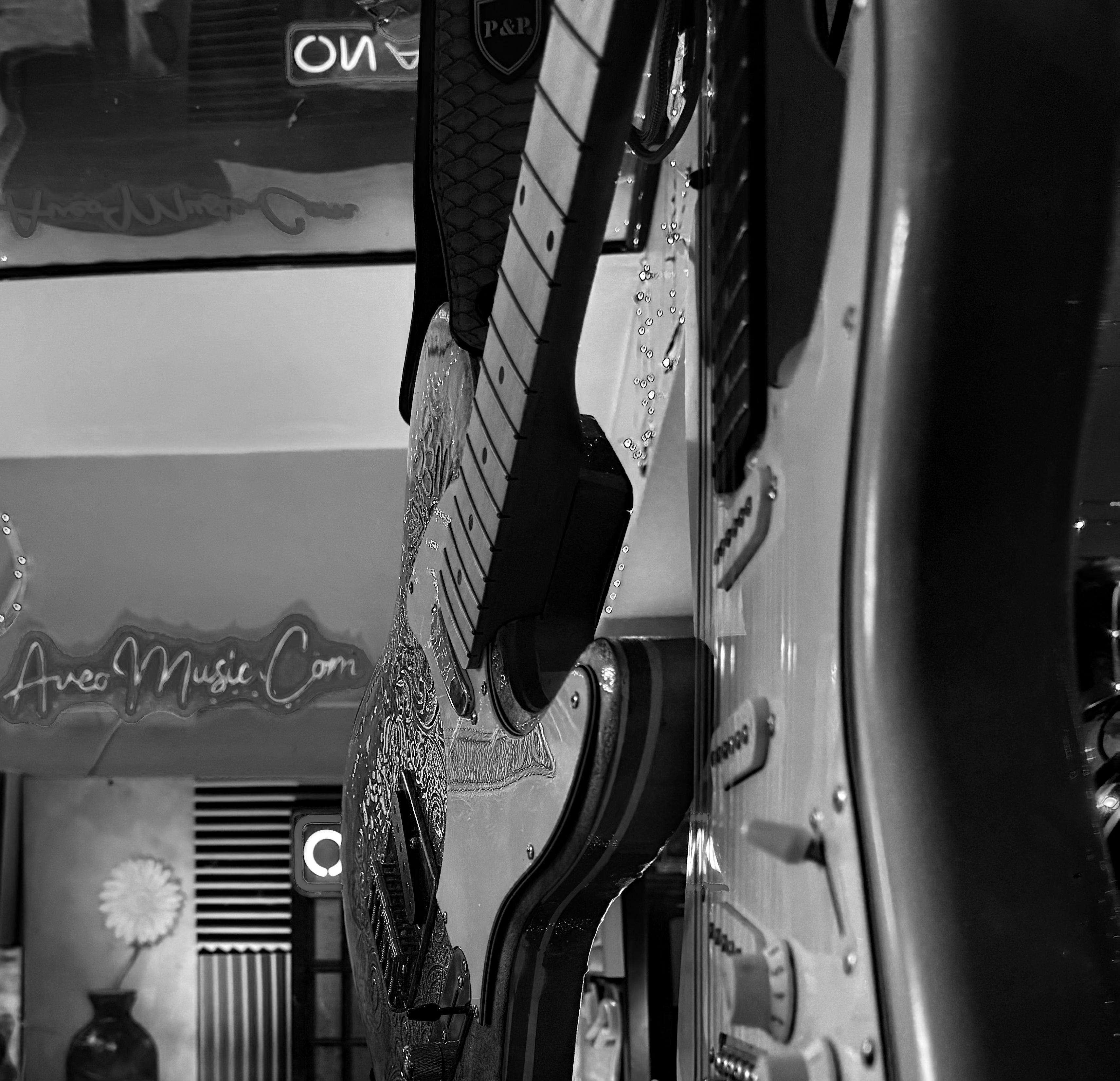 A black and white closeup view of a couple of guitars in the distance you can read AveoMusic.com in neon lights